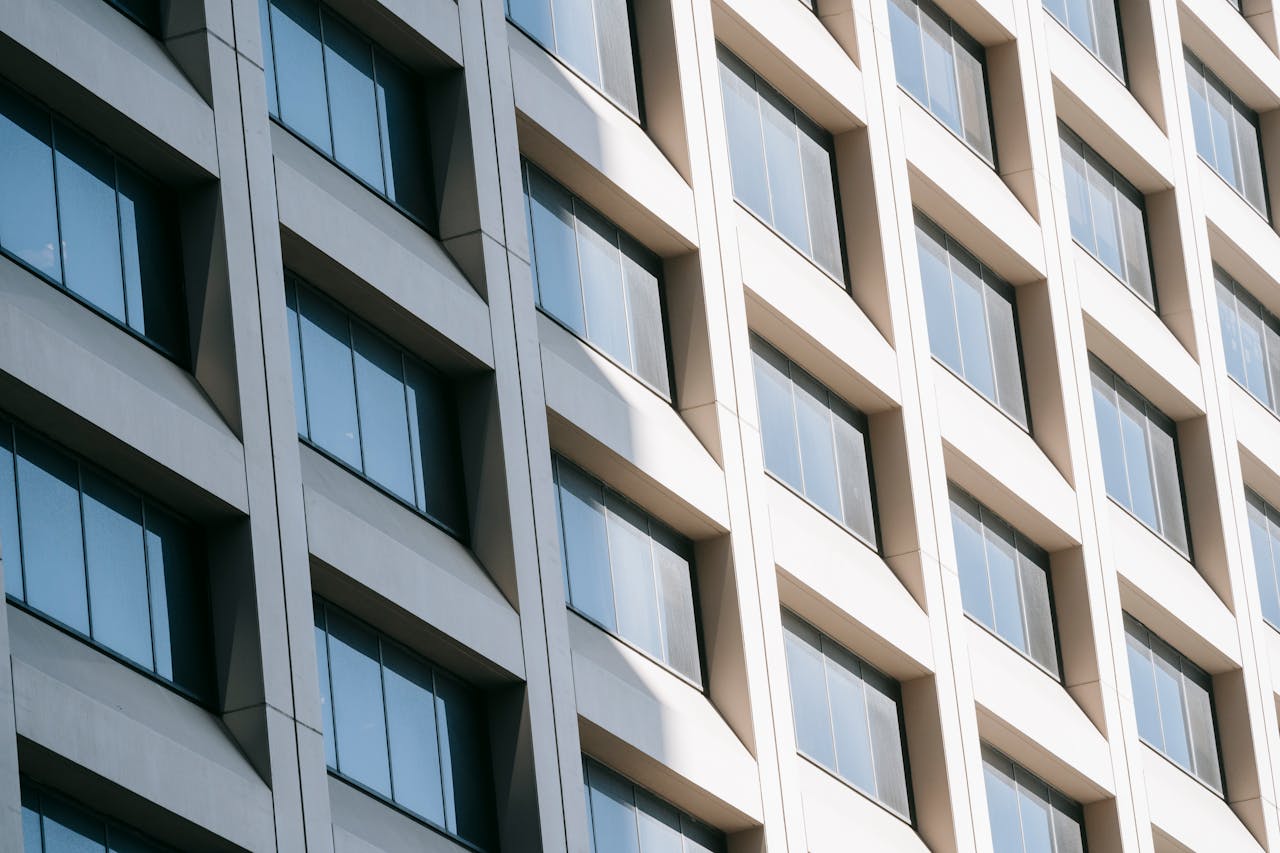 Low angle of rows of modern glass windows on facade of contemporary white multistory building reflecting sunlight